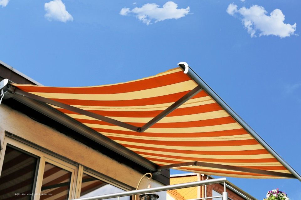 JK Fußbodenbau und Raumausstattung GmbH & Co. KG – eine rot-weiße Markise vor einem blauen Himmel