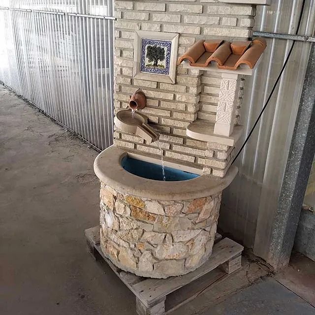 Una fuente de piedra se encuentra sobre una paleta de madera al lado de una pared de ladrillos.
