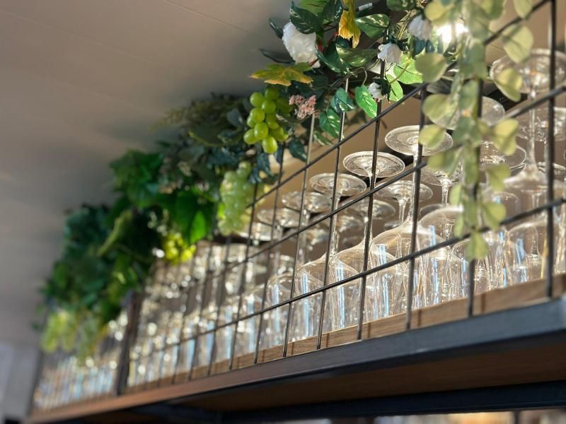 Ein Regal voller Weingläser und Pflanzen, die von der Decke hängen.