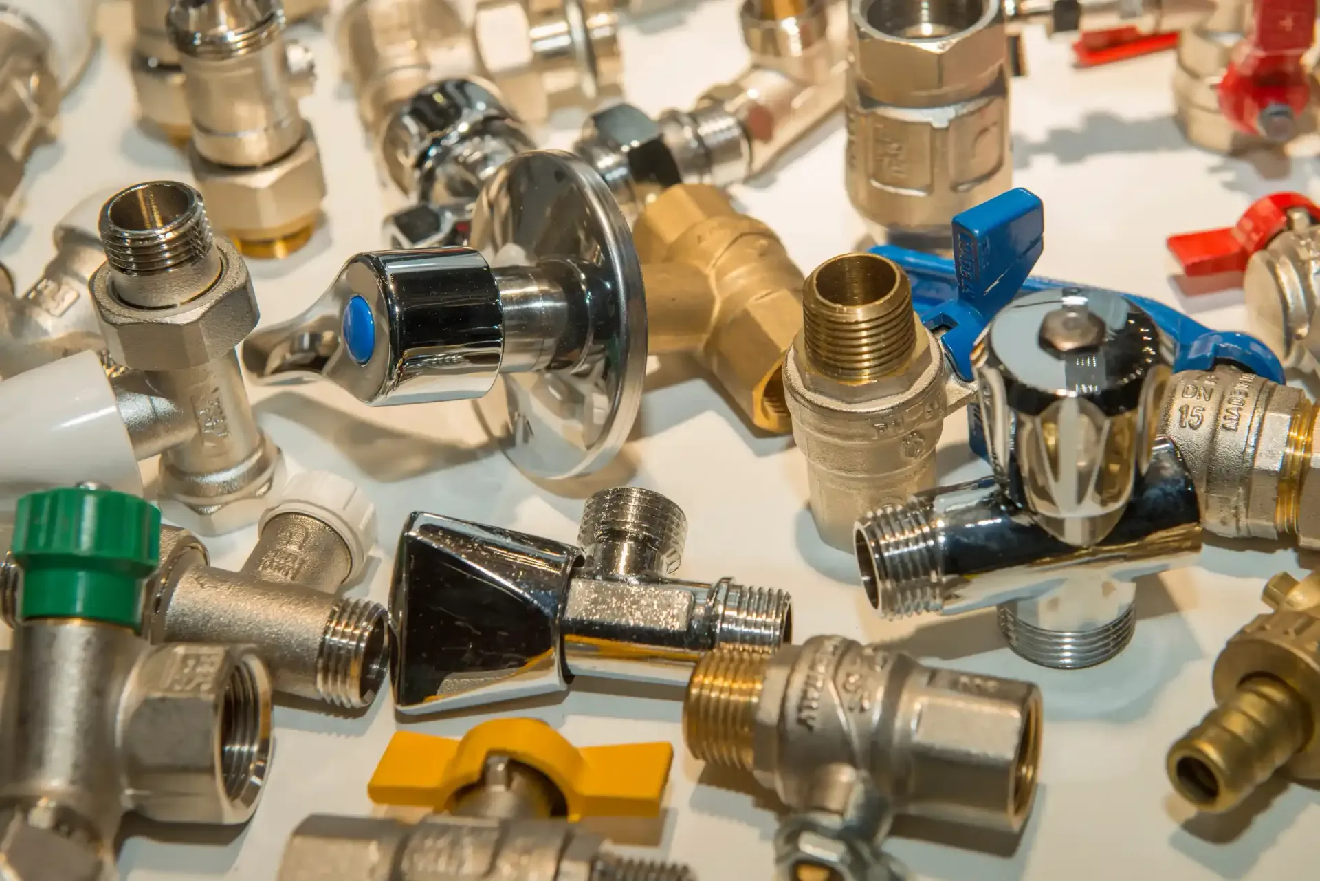 Un montón de válvulas, accesorios y conectores de fontanería de latón y cromo sobre una superficie blanca.