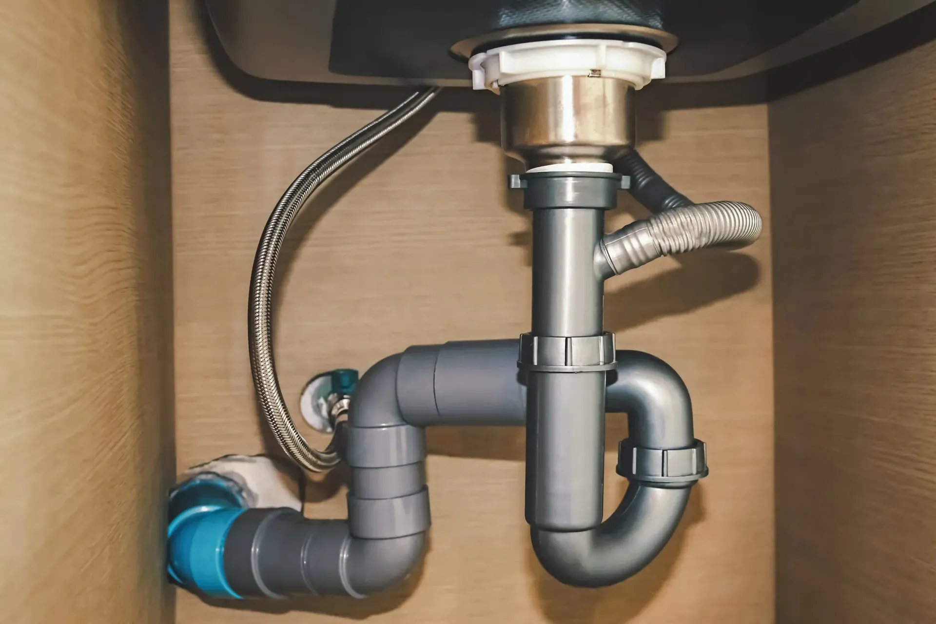 Tuberías de desagüe de PVC gris dispuestas en forma de sifón bajo un mueble de fregadero.