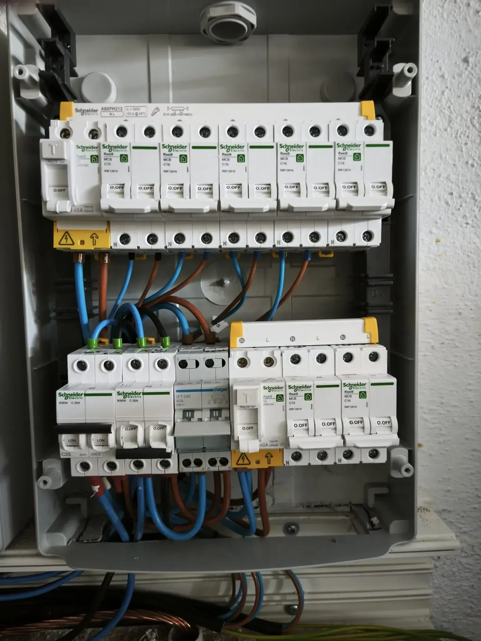 Un cuadro eléctrico residencial abierto con varios disyuntores blancos y cableado azul y marrón.