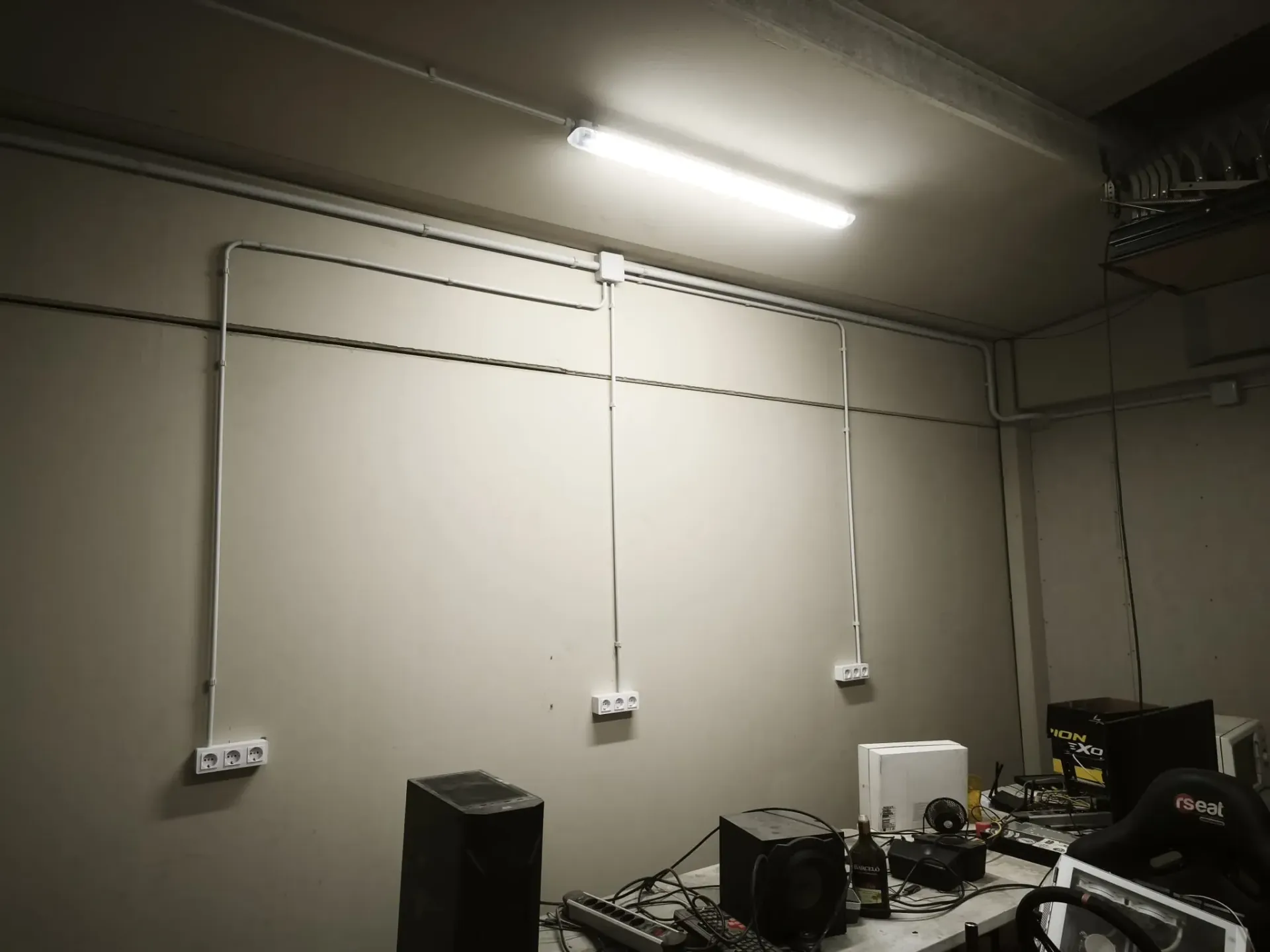 Una habitación iluminada con paredes blancas, cableado eléctrico a la vista 