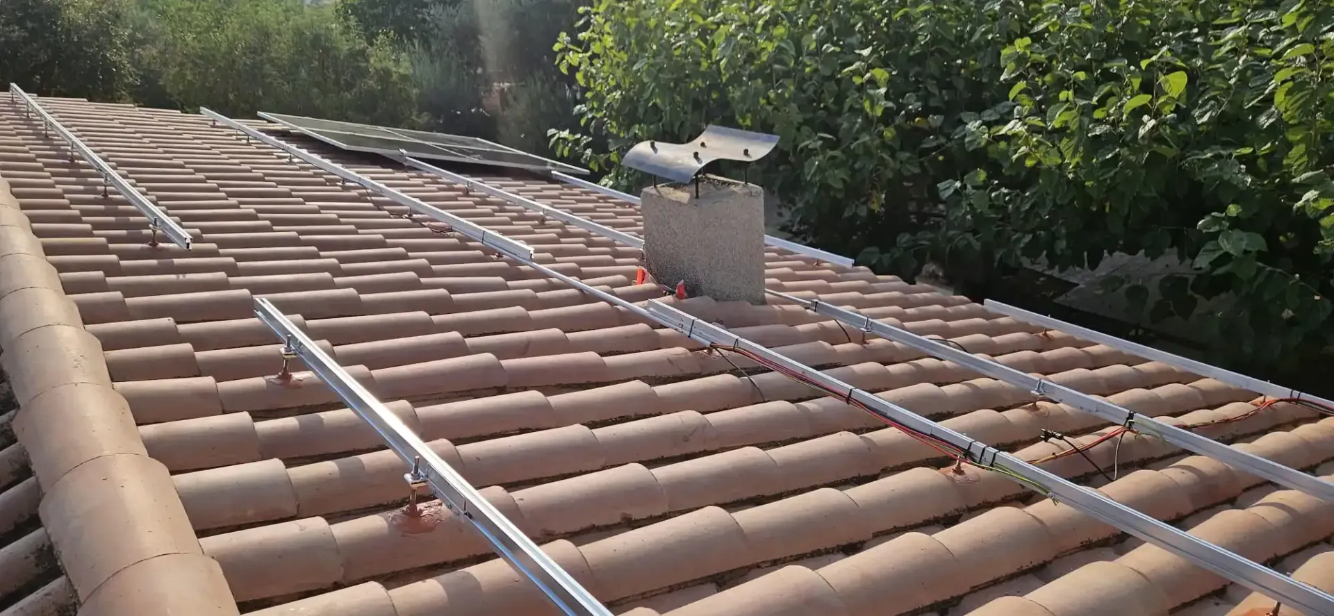 Rieles de montaje metálicos para paneles solares instalados en un tejado de tejas de terracota con un tubo de ventilación.