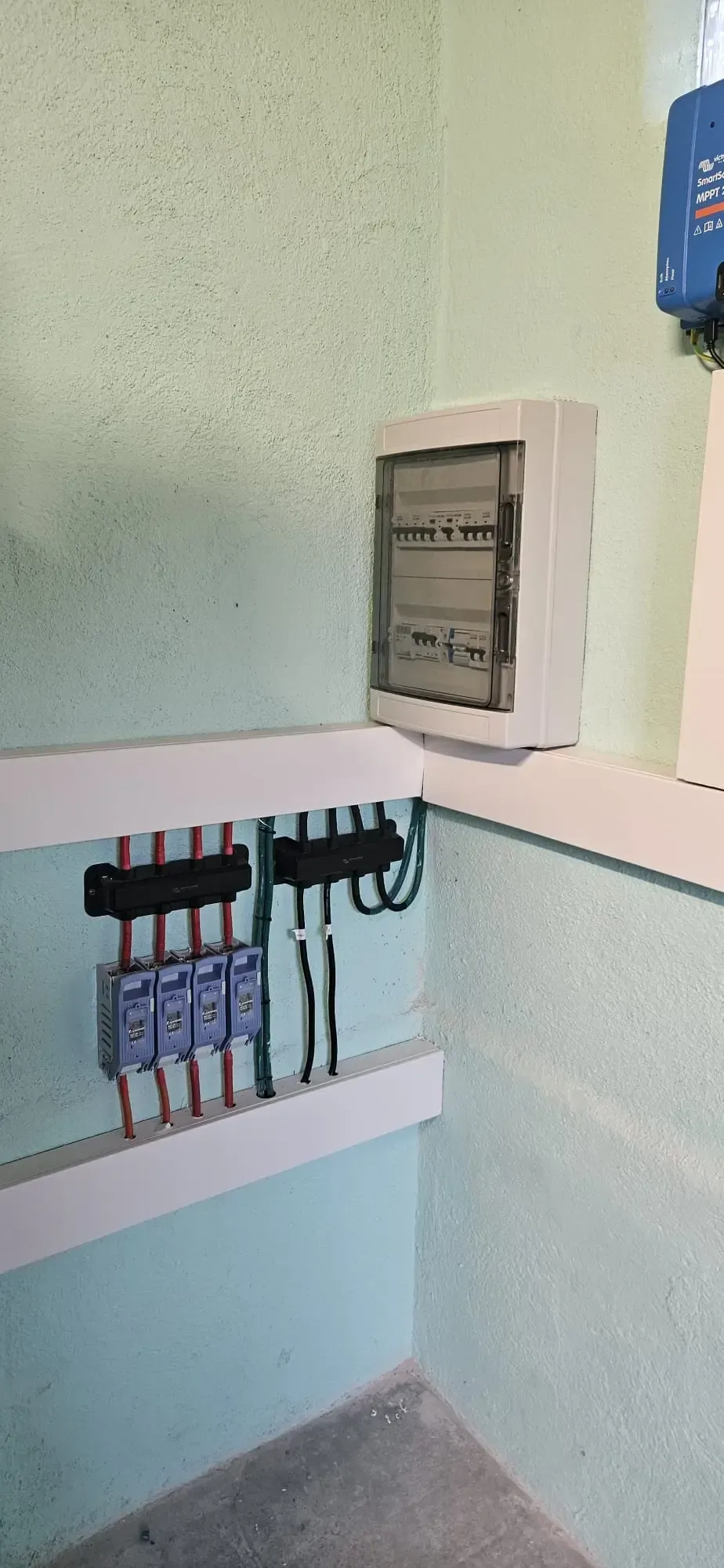 Cableado eléctrico y cuadro de distribución montados en una pared de color verde claro sobre un suelo de hormigón.