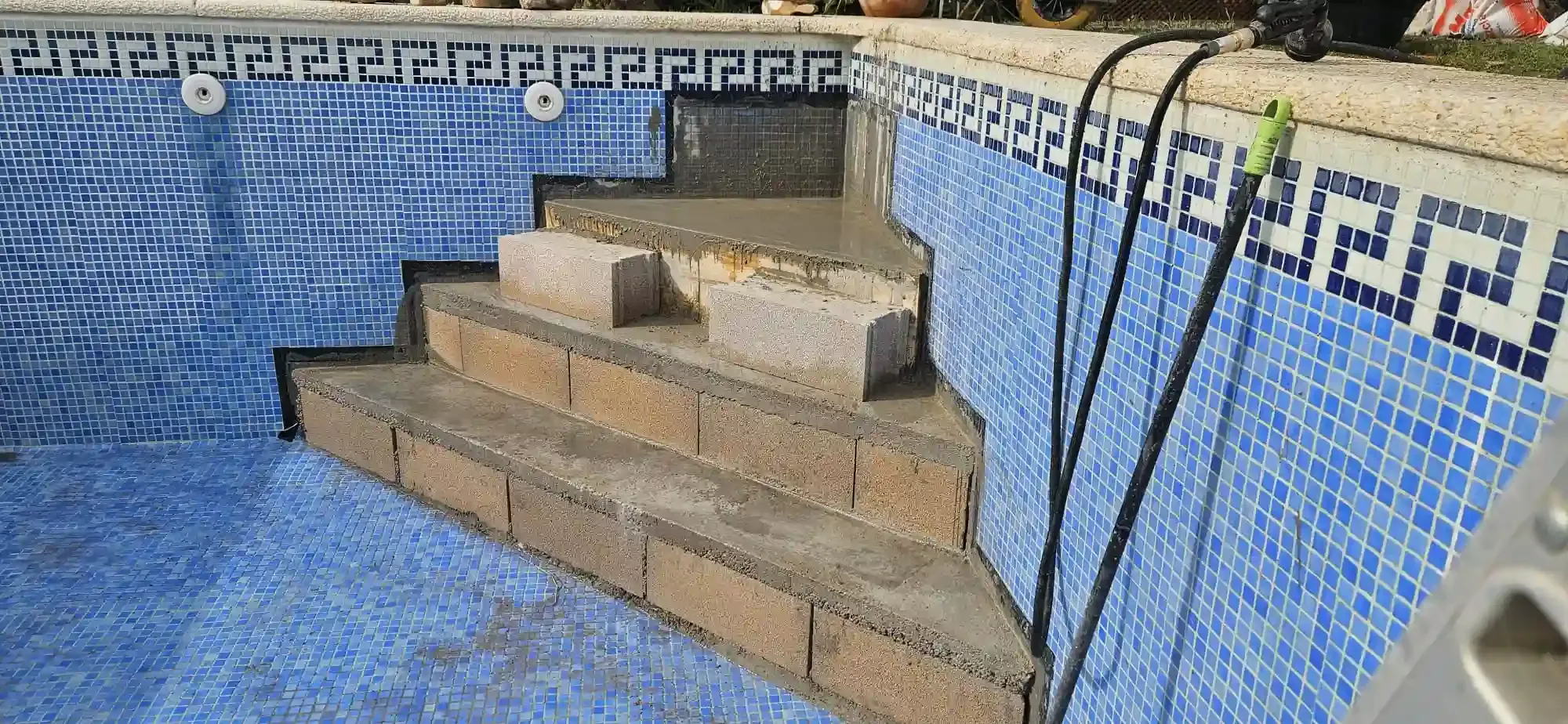 Escaleras de hormigón en construcción en una piscina con azulejos azules y un borde decorativo oscuro en el borde superior.