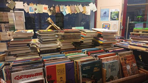 Des piles de bandes dessinées et de magazines remplissent l'étalage d'une librairie, avec une rangée de petites cartes suspendues au-dessus par une ficelle.