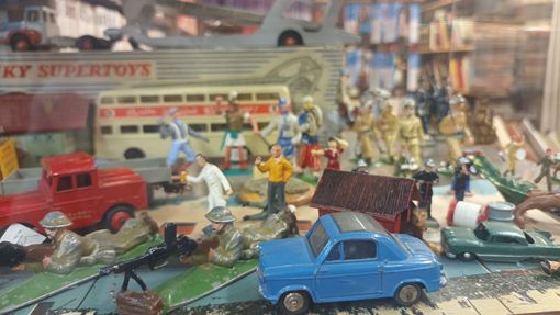 Une exposition de véhicules jouets anciens et de figurines miniatures, comprenant un camion rouge, une voiture bleue et un bus blanc à impériale.