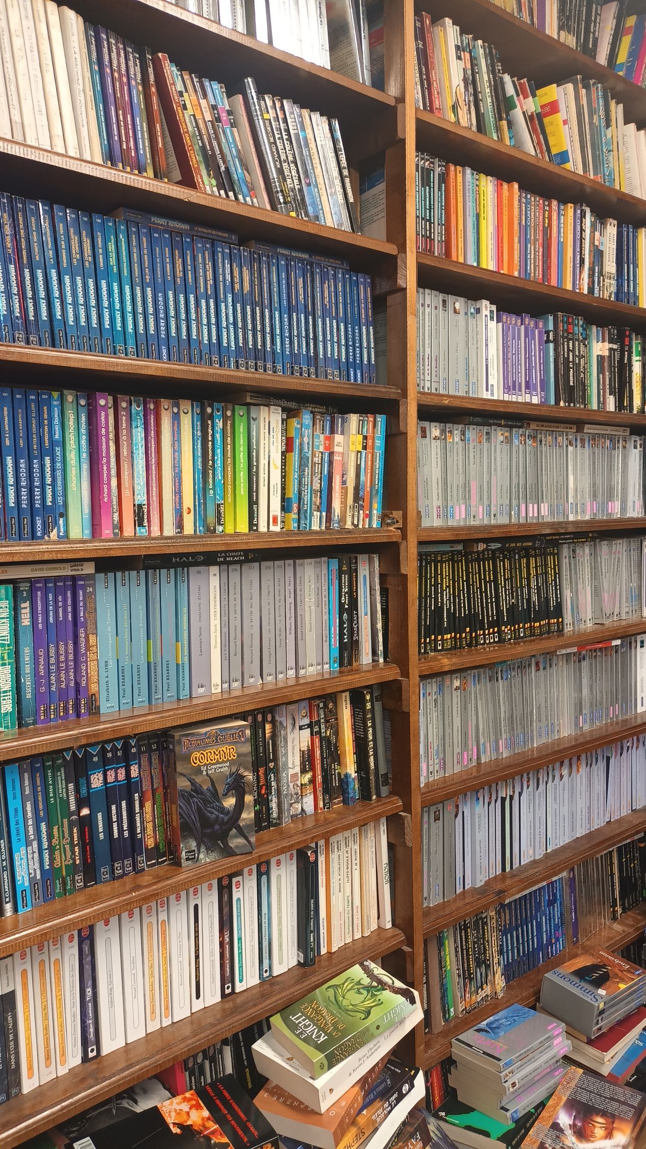 De hautes étagères en bois remplies d'une grande collection de livres colorés et de boîtiers multimédias, certains empilés horizontalement.