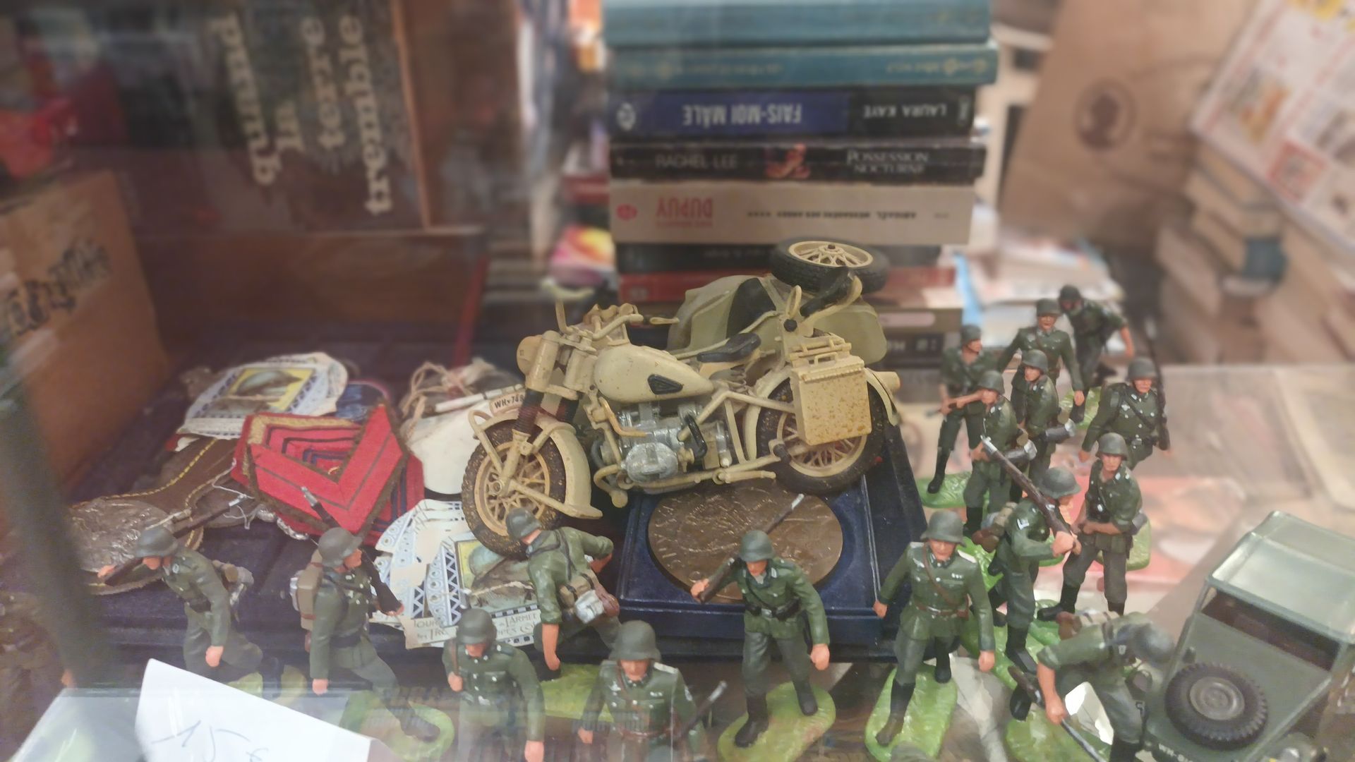 Une étagère expose une moto miniature avec side-car, entourée d'un groupe de petites figurines militaires vertes.