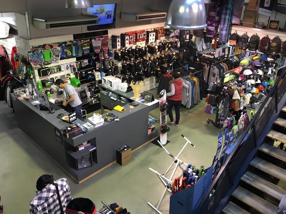 Dans un magasin de ski, clients et employés interagissent près d'une caisse, entourés de marchandises.