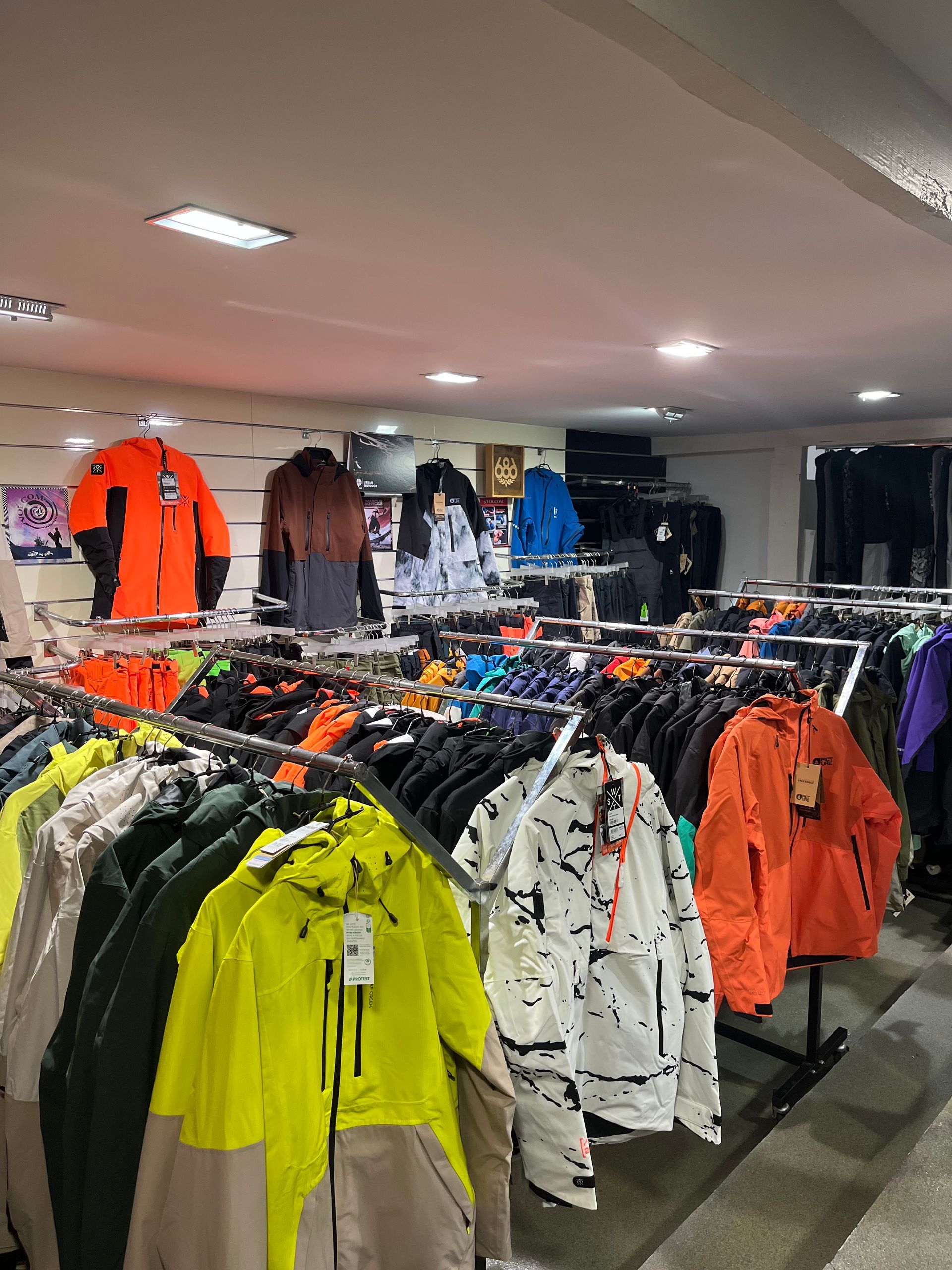 Intérieur d'un magasin de vêtements avec des portants de vestes de différentes couleurs, notamment orange, jaune et noir.