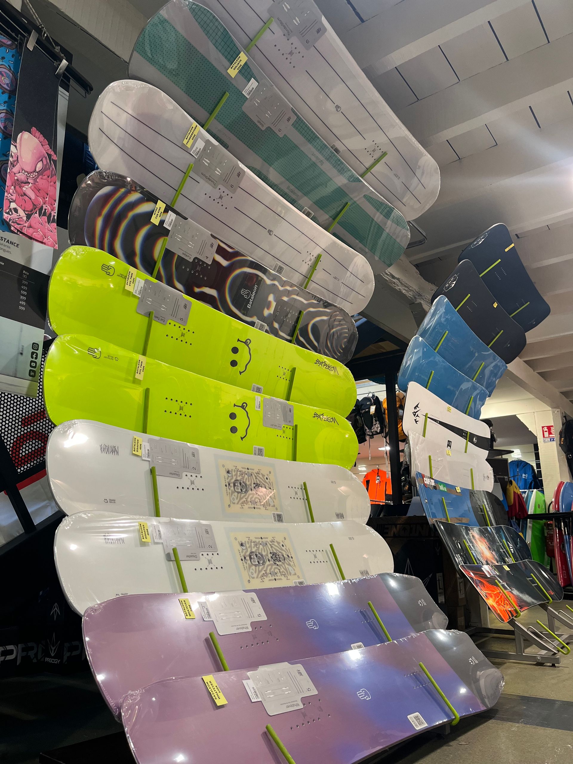 Des planches de snowboard de couleurs et de modèles variés, empilées dans un magasin et appuyées contre un mur.