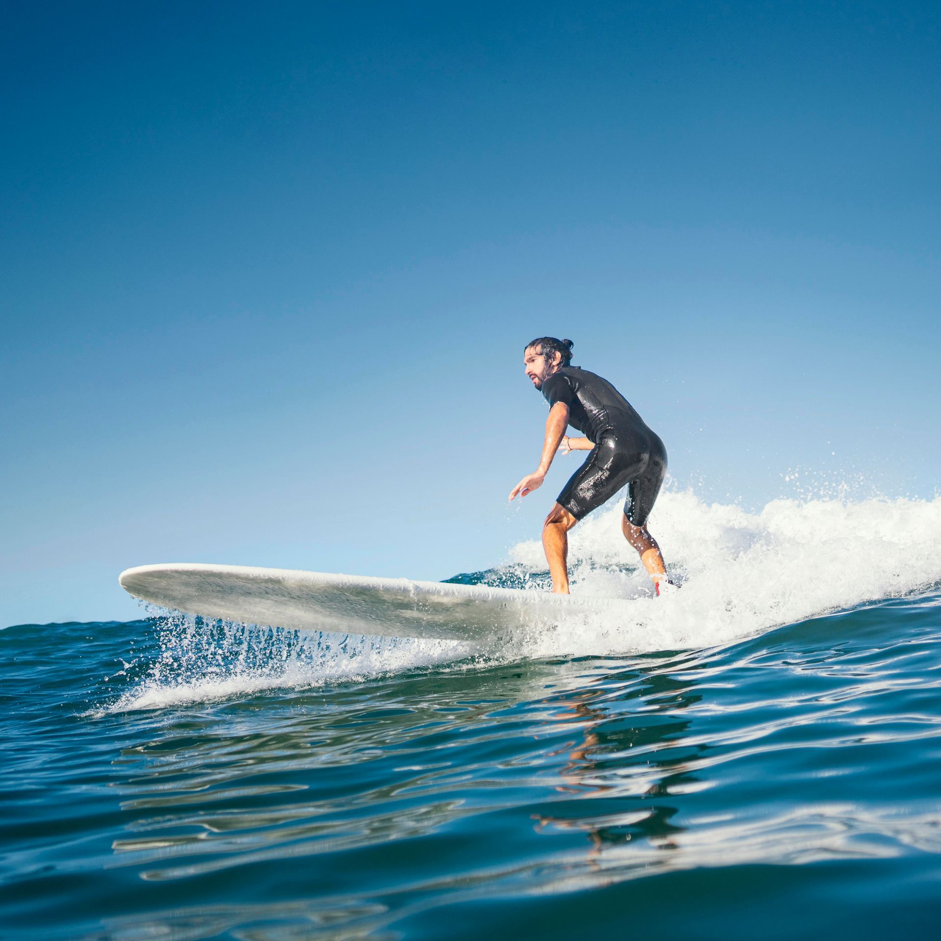 Une personne surfe sur une longue planche blanche dans l'océan. Ciel bleu clair.