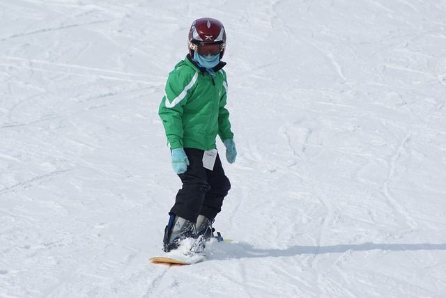 Une personne fait du snowboard sur une pente enneigée, portant une veste verte, un casque et des gants bleus.