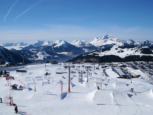 Station de ski enneigée avec tremplins et obstacles. Montagnes en arrière-plan, ciel bleu azur.