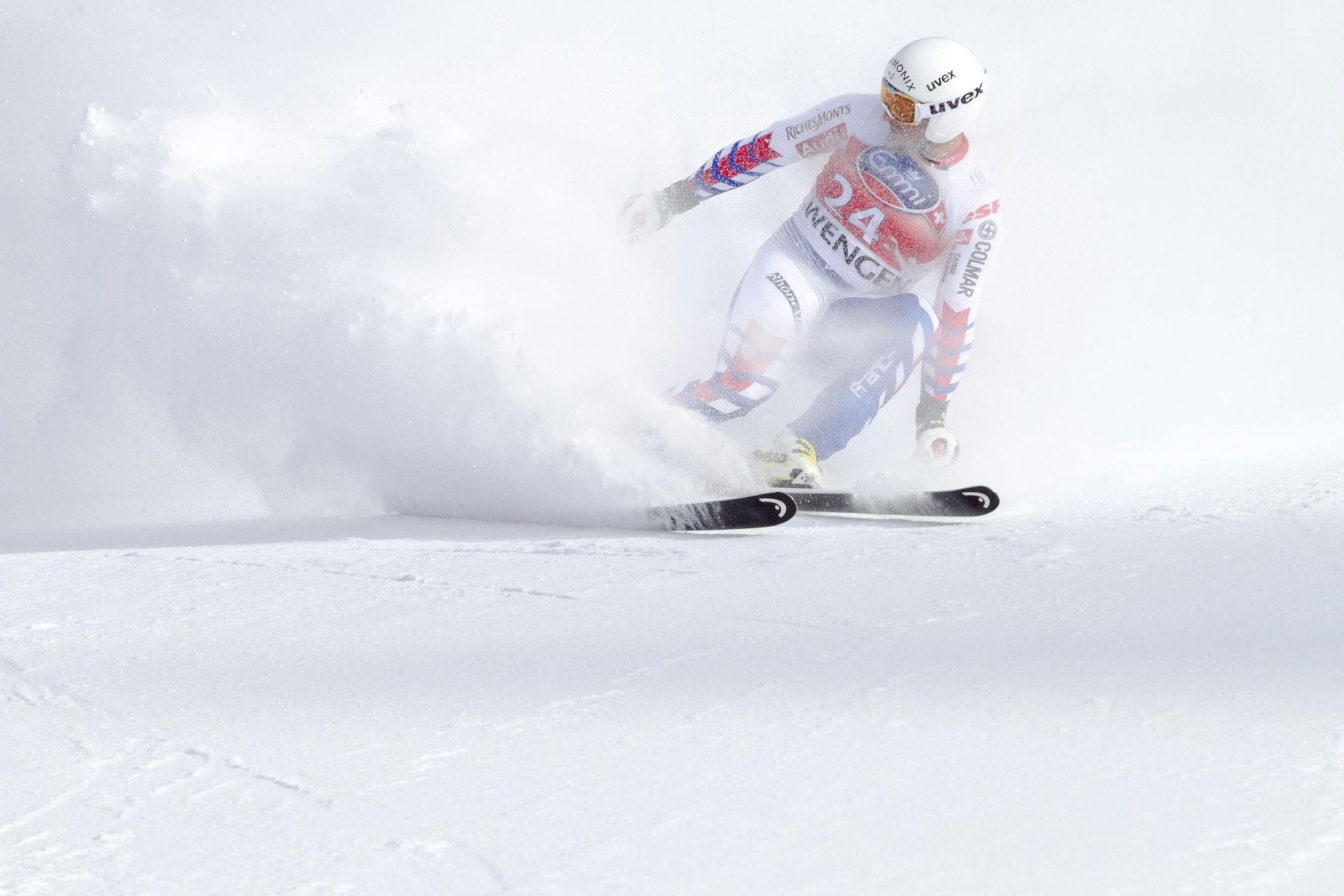 Un skieur carve sur une pente enneigée, soulevant un nuage de neige.