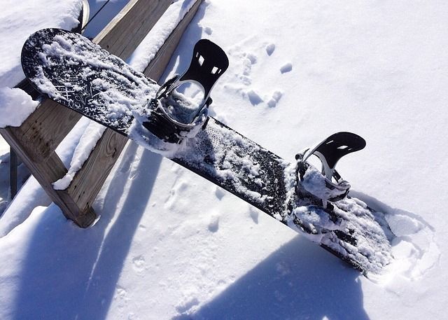 Une planche de snowboard recouverte de neige, posée sur un banc en bois, dans un décor enneigé.