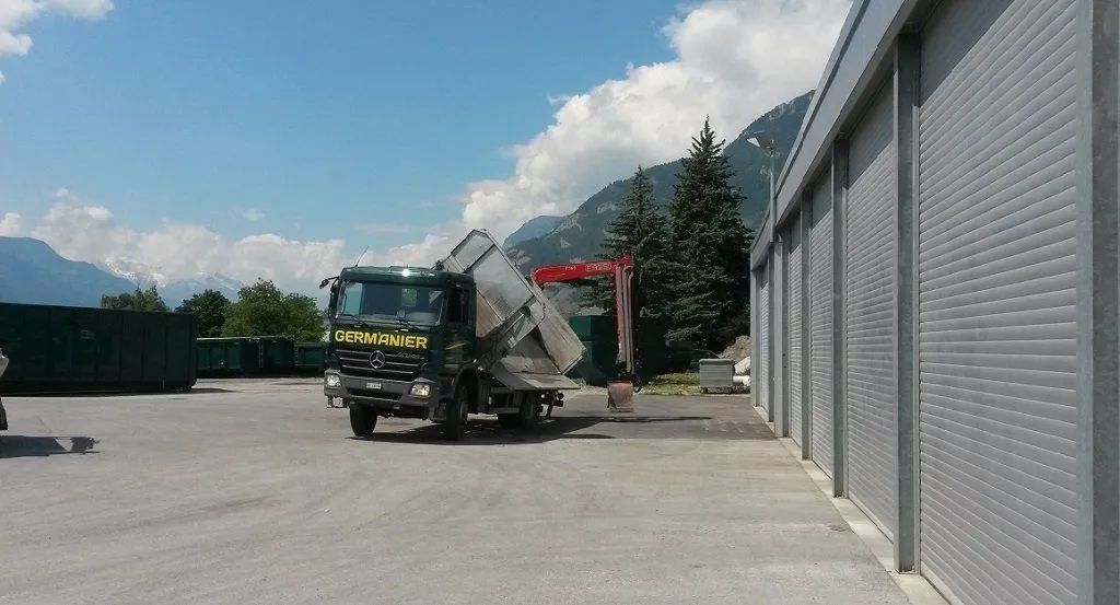 Un camion à benne basculante est garé sur un parking à côté d'un bâtiment.