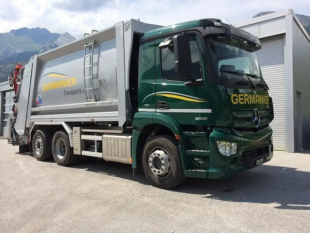 Un camion poubelle vert est garé devant un bâtiment.