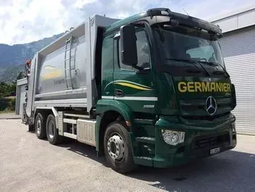 Un camion poubelle vert est garé devant un bâtiment.