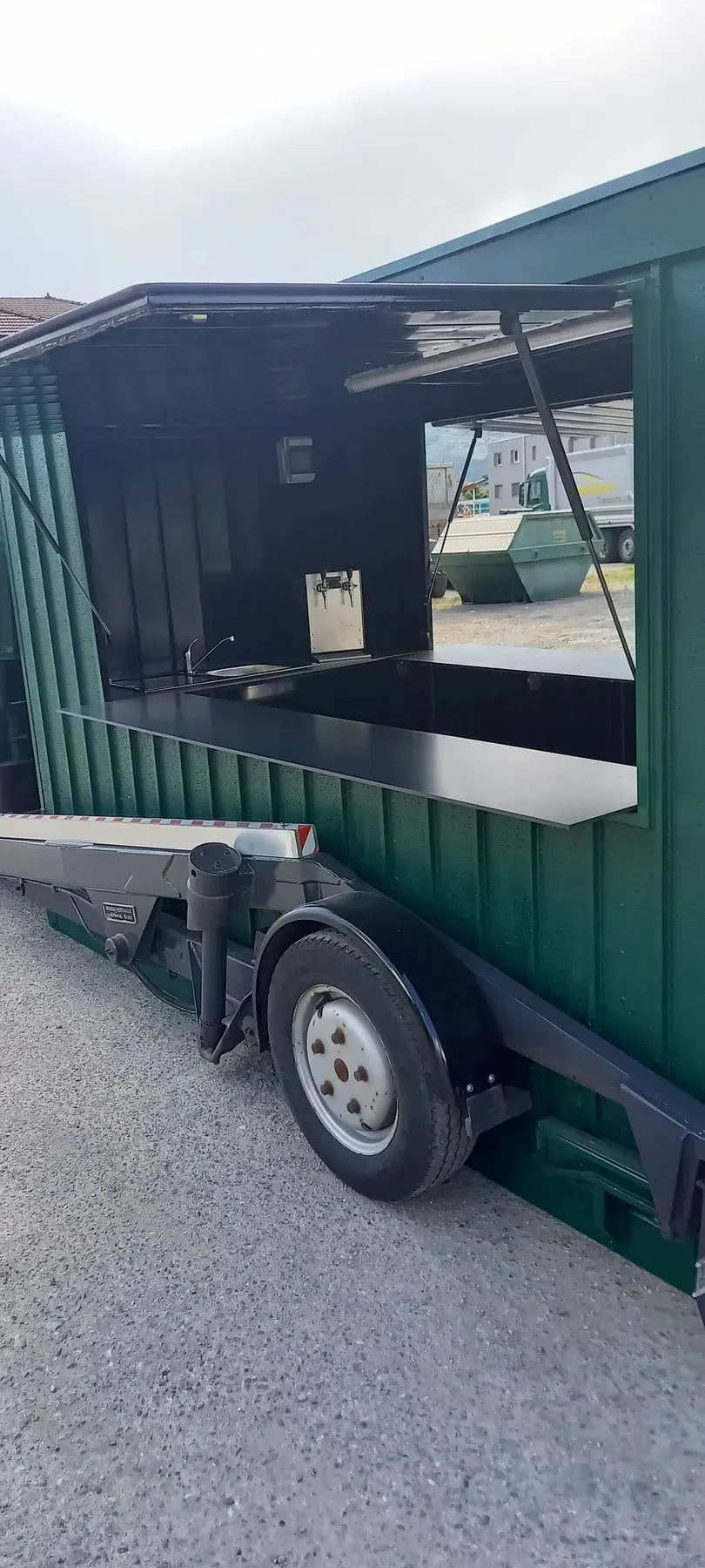 Un food truck vert est garé sur un terrain en gravier.