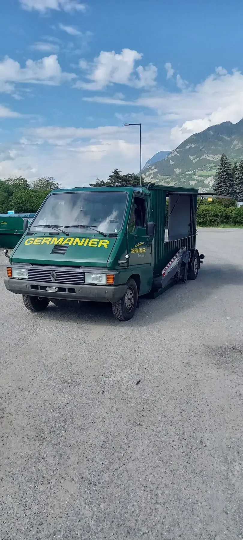 Une camionnette verte et jaune est garée sur un terrain en gravier.