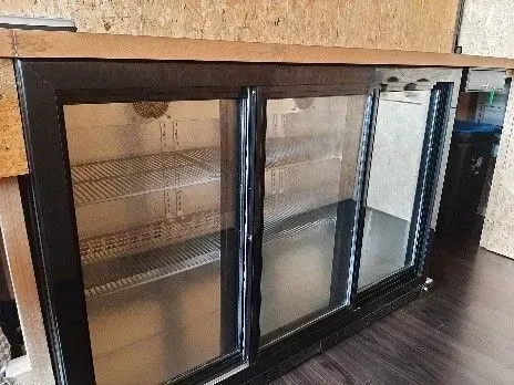 Un réfrigérateur à porte coulissante en verre est posé sur un plancher en bois.