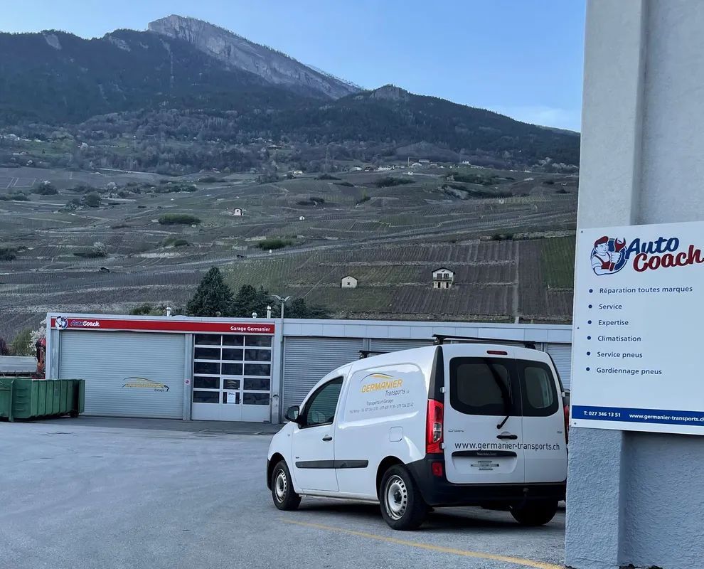 Une camionnette blanche est garée devant un bâtiment avec une montagne en arrière-plan.