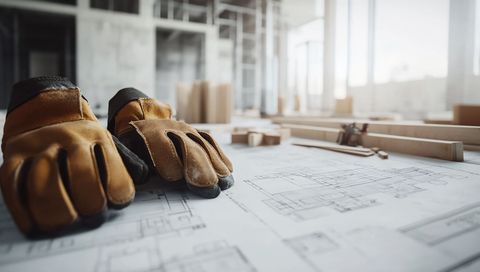 Gants de travail sur des plans d'architecte à un bureau de chantier baigné de soleil.