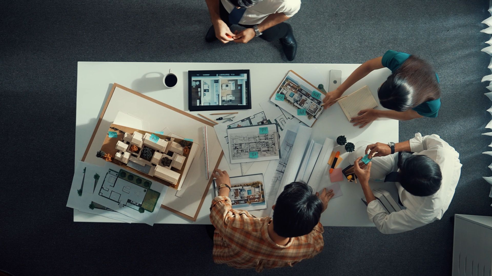 Vue aérienne de quatre personnes collaborant autour d'une table blanche avec des papiers, des appareils et des outils.