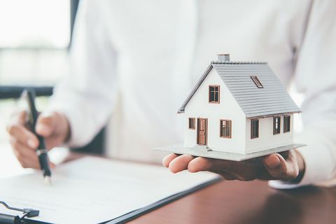 Une personne tenant une maquette de maison à côté d'un bloc-notes et d'un stylo.