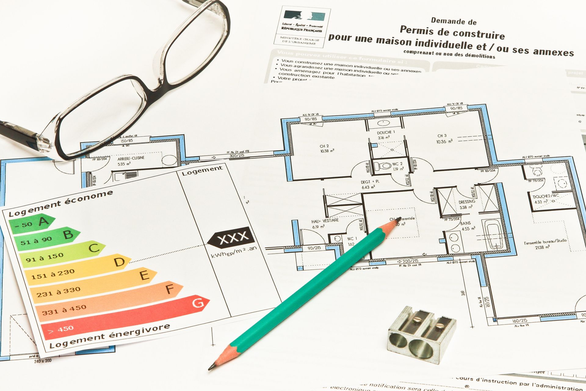 Plan d'architecture avec lunettes, crayon, tableau des étiquettes énergétiques et calculatrice sur un bureau.