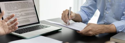 Deux personnes en réunion, examinant des documents, avec un ordinateur portable et un bloc-notes sur un bureau.