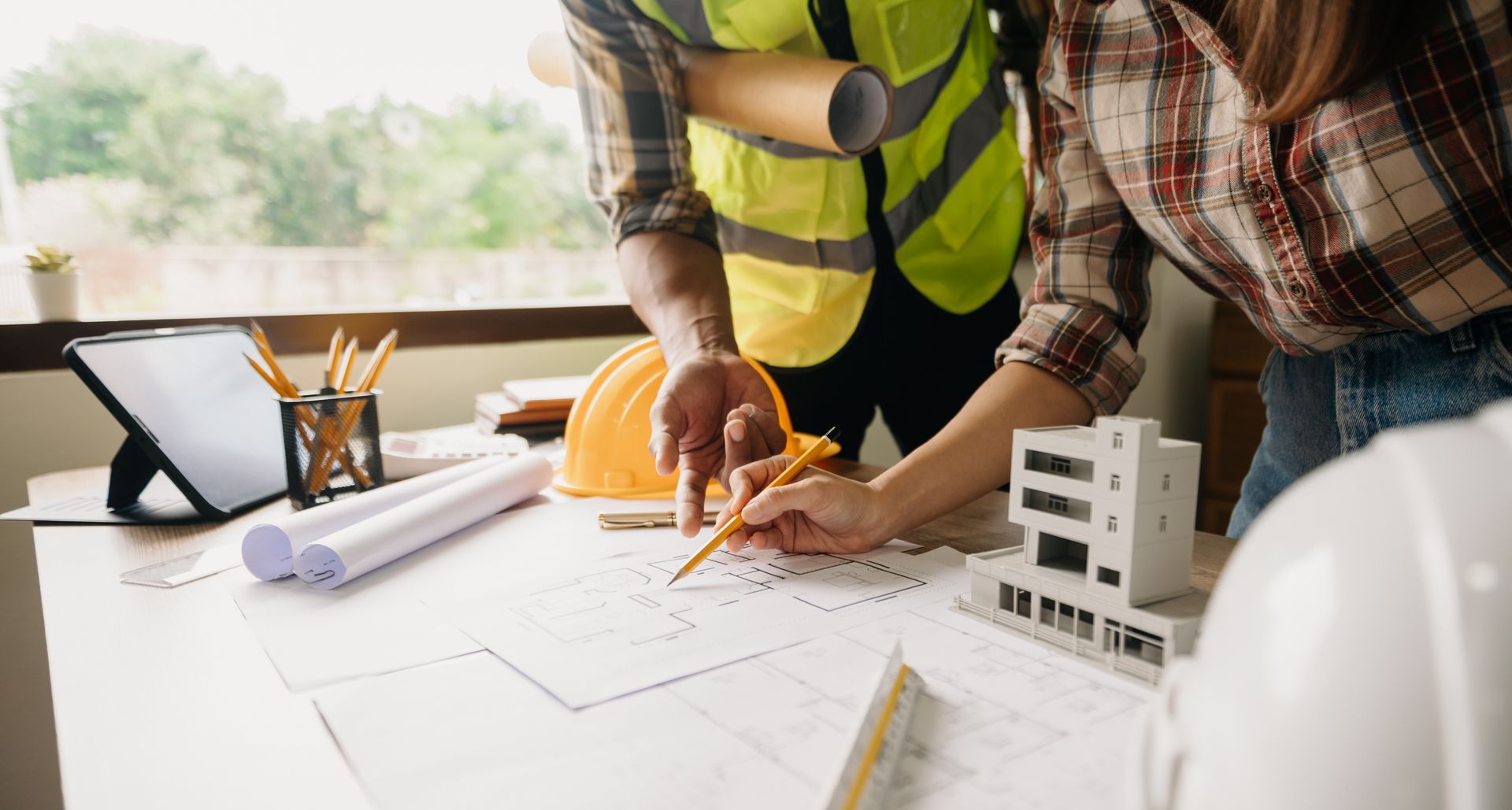 Des personnes examinant des plans et une maquette sur un chantier de construction, portant des gilets de sécurité et des casques de chantier.