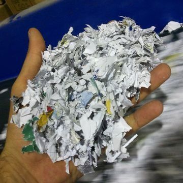Una mano sosteniendo un montón de papel blanco triturado con trocitos de colores a la vista.