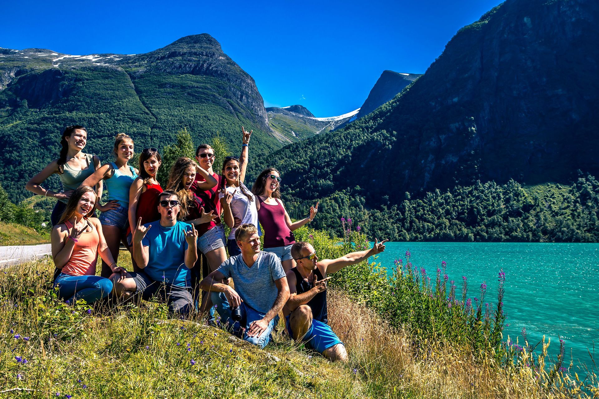 Groupe de personnes posant au bord d'un lac turquoise avec des montagnes en arrière-plan.