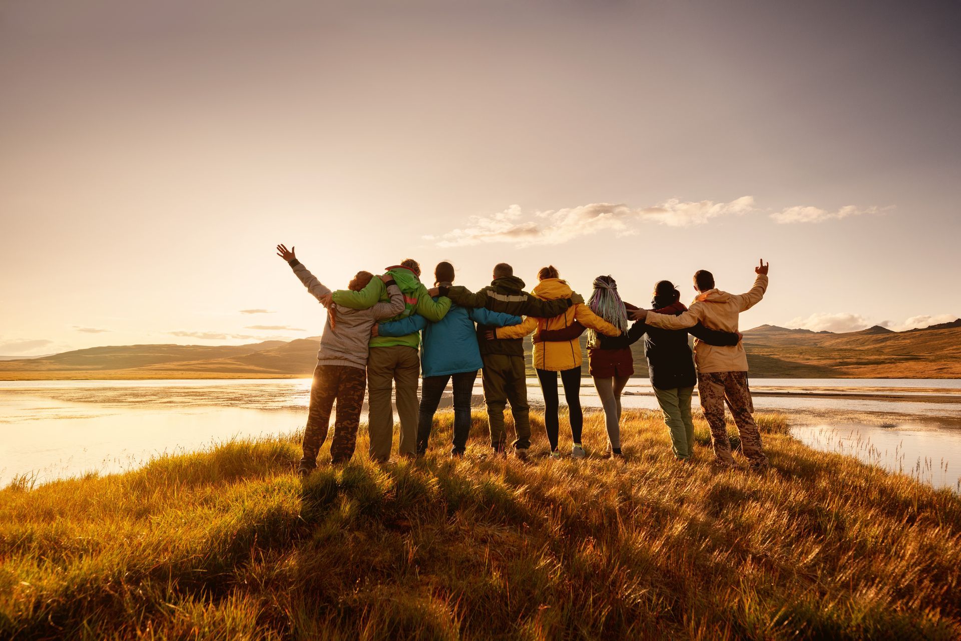 Groupe de personnes enlacées, face à un coucher de soleil sur l'eau.