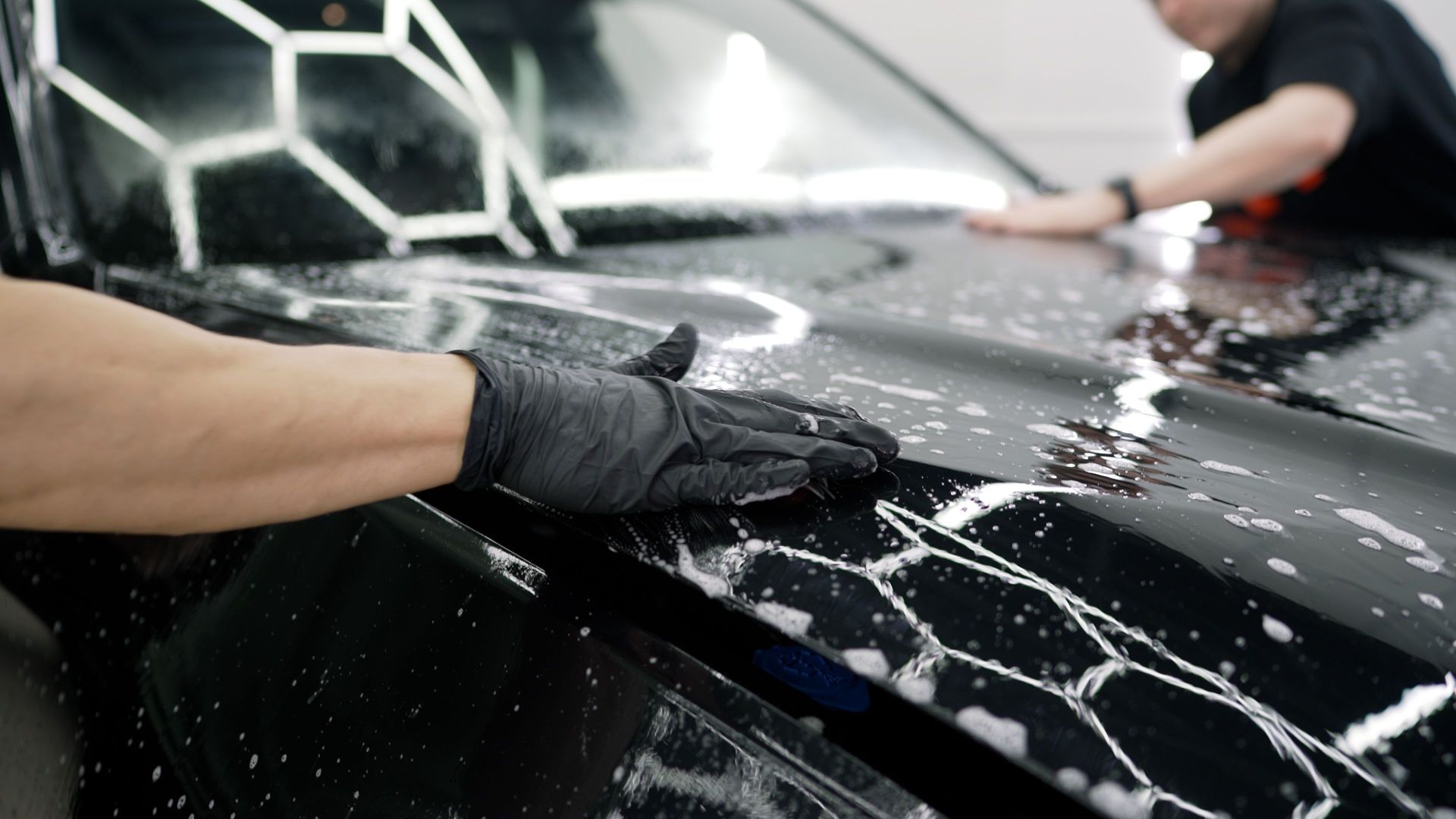 Une main avec un gant noir en train de laver le capot d'une voiture noire