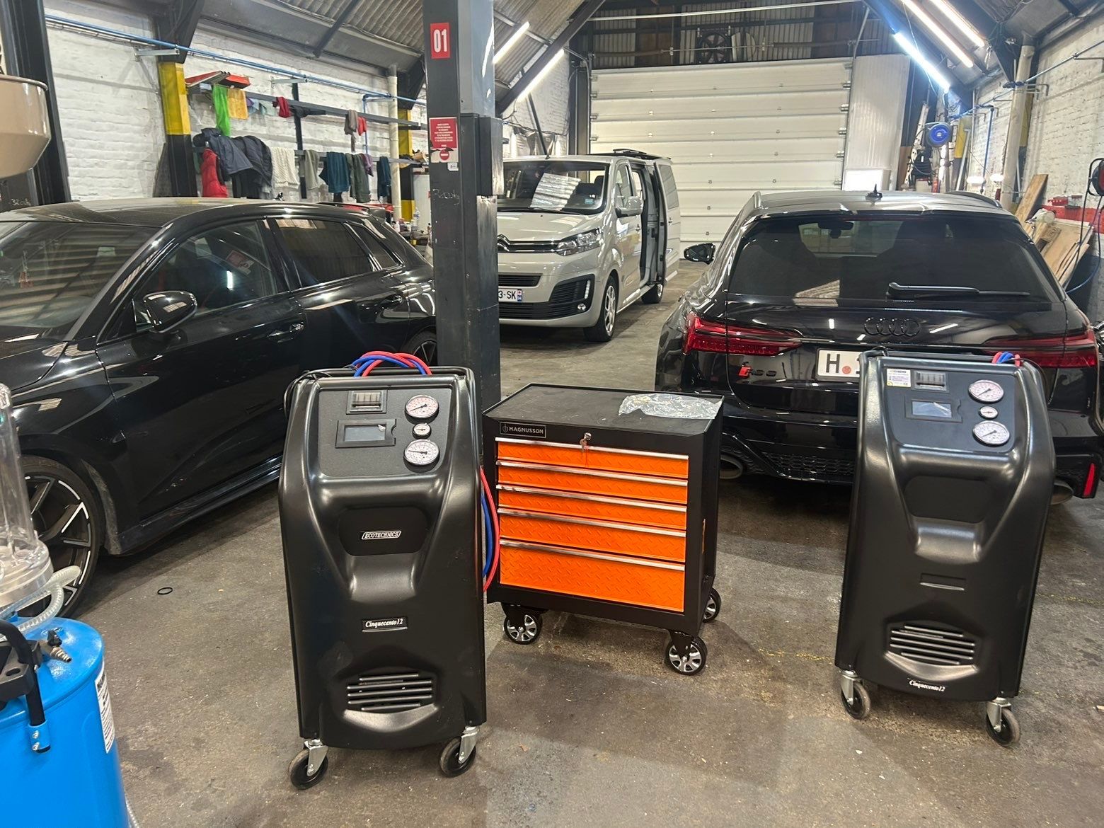 Dans un atelier de réparation automobile professionnel, deux machines d'entretien de climatisation automobile entourent une armoire à outils orange.