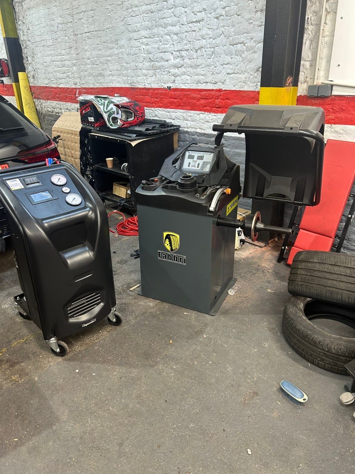 Une machine à pneus Redats rouge se trouve dans un atelier de réparation automobile, des pneus à proximité.