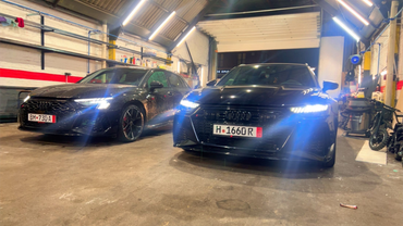 Dans un garage, une machine professionnelle pour changer les pneus est installée, entourée de pneus de voiture en vrac et d'une jante sur son plateau tournant.