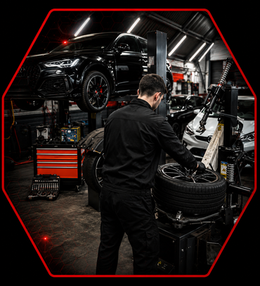 Dans un garage, une machine professionnelle pour changer les pneus est installée, entourée de pneus de voiture en vrac et d'une jante sur son plateau tournant.