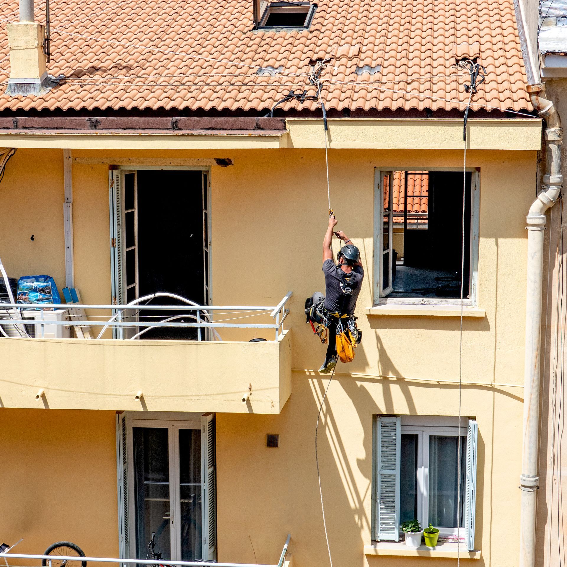 Un cordiste descend en rappel la façade d'une maison jaune en rénovation.