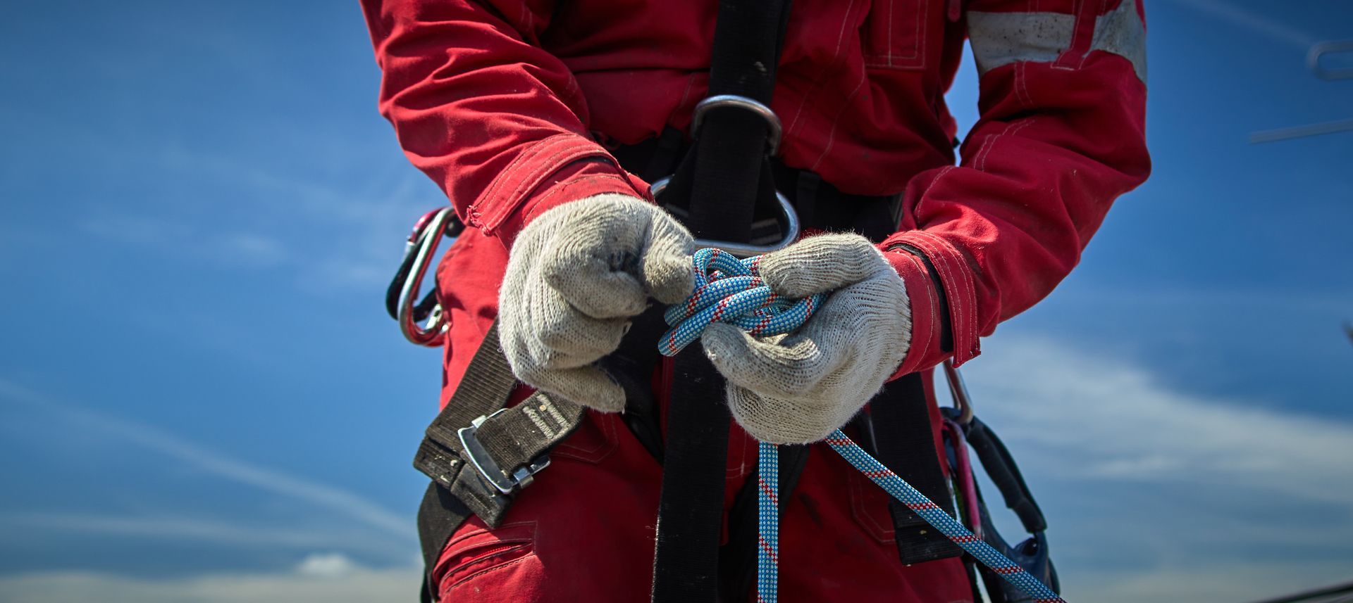Grimpeur en veste et gants rouges tenant une corde bleue.