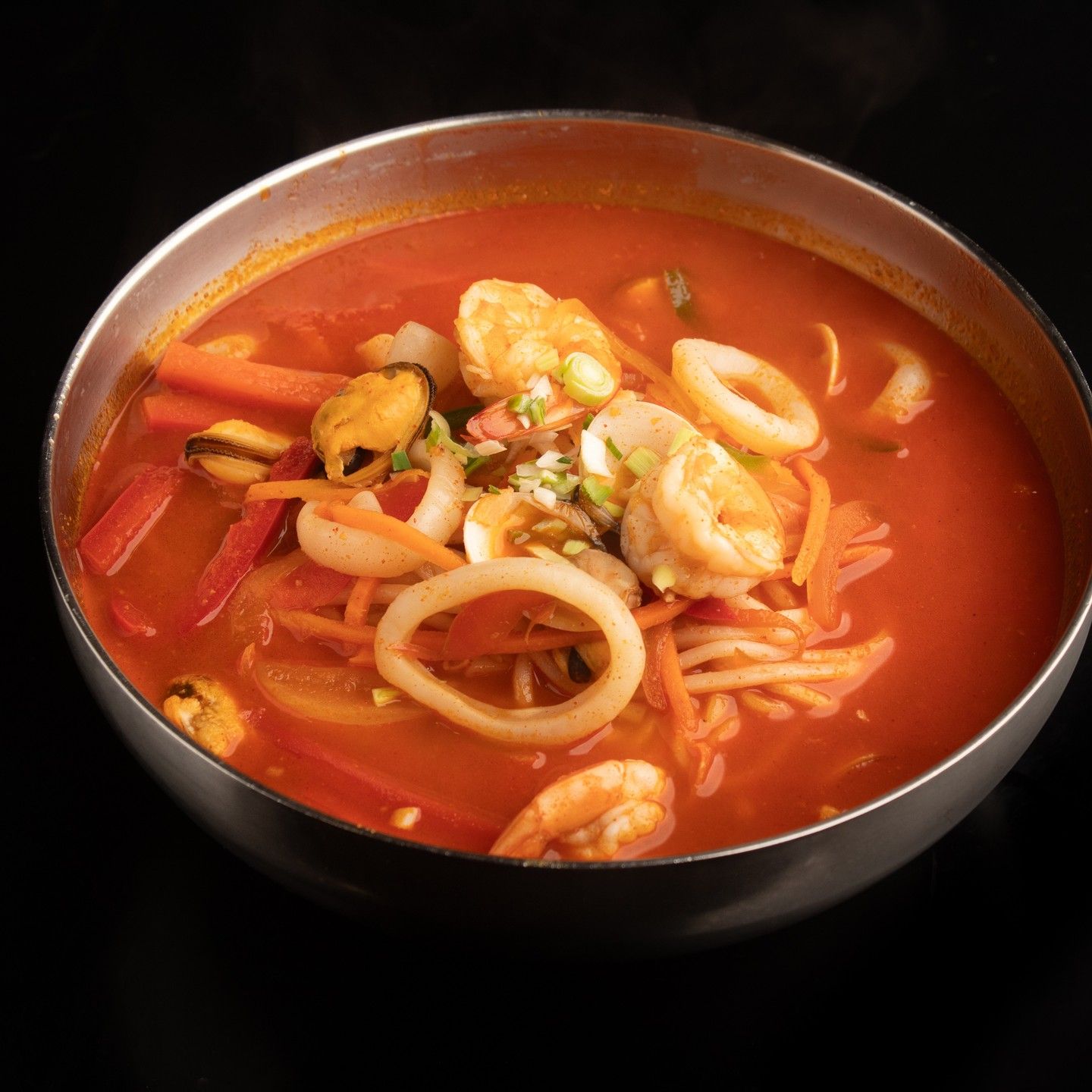 Cuenco de sopa de fideos con mariscos en caldo rojo, con camarones y aros de calamar, sobre un fondo oscuro