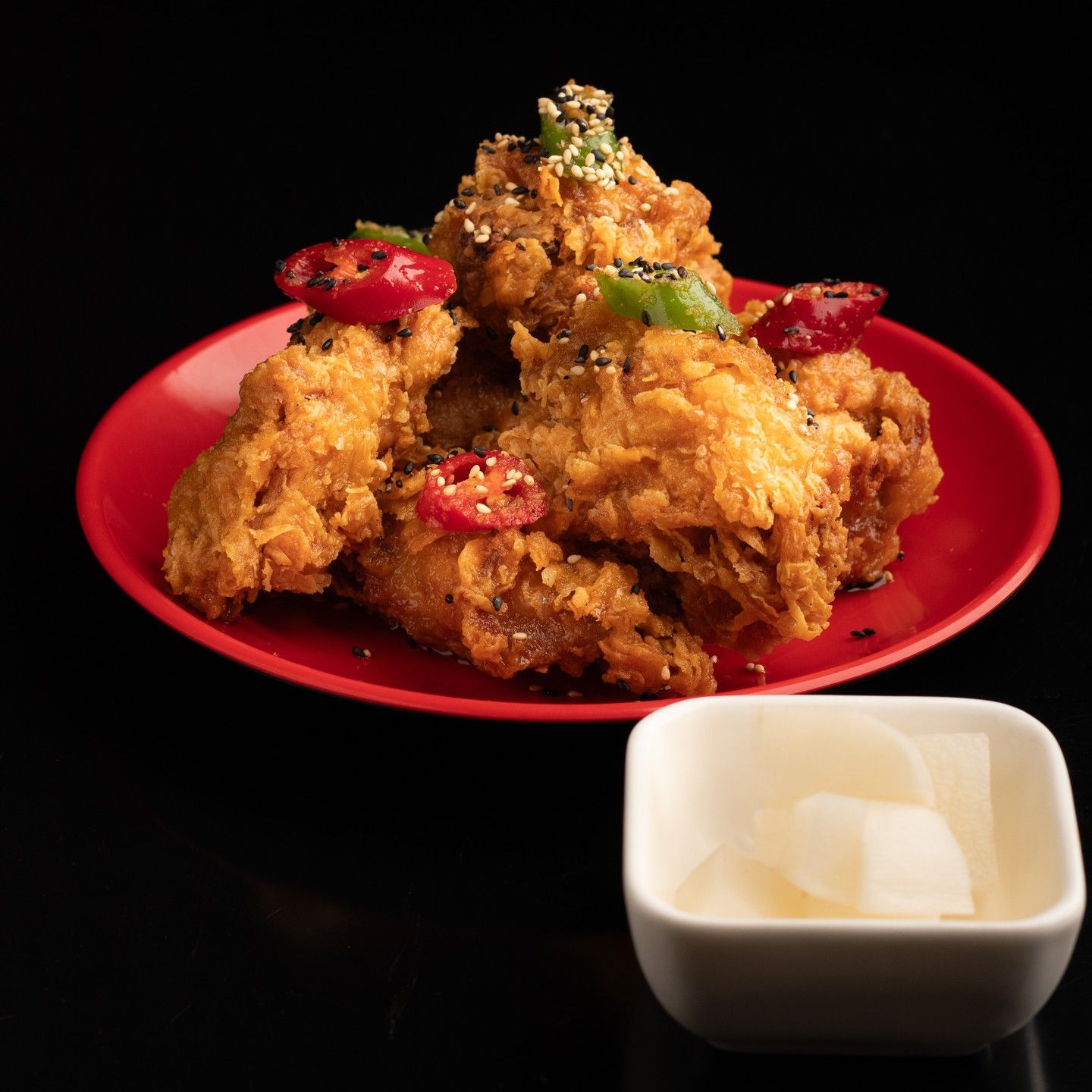 Plato rojo de pollo frito crujiente cubierto con chiles rojos y verdes, con un cuenco pequeño de cubitos al lado.
