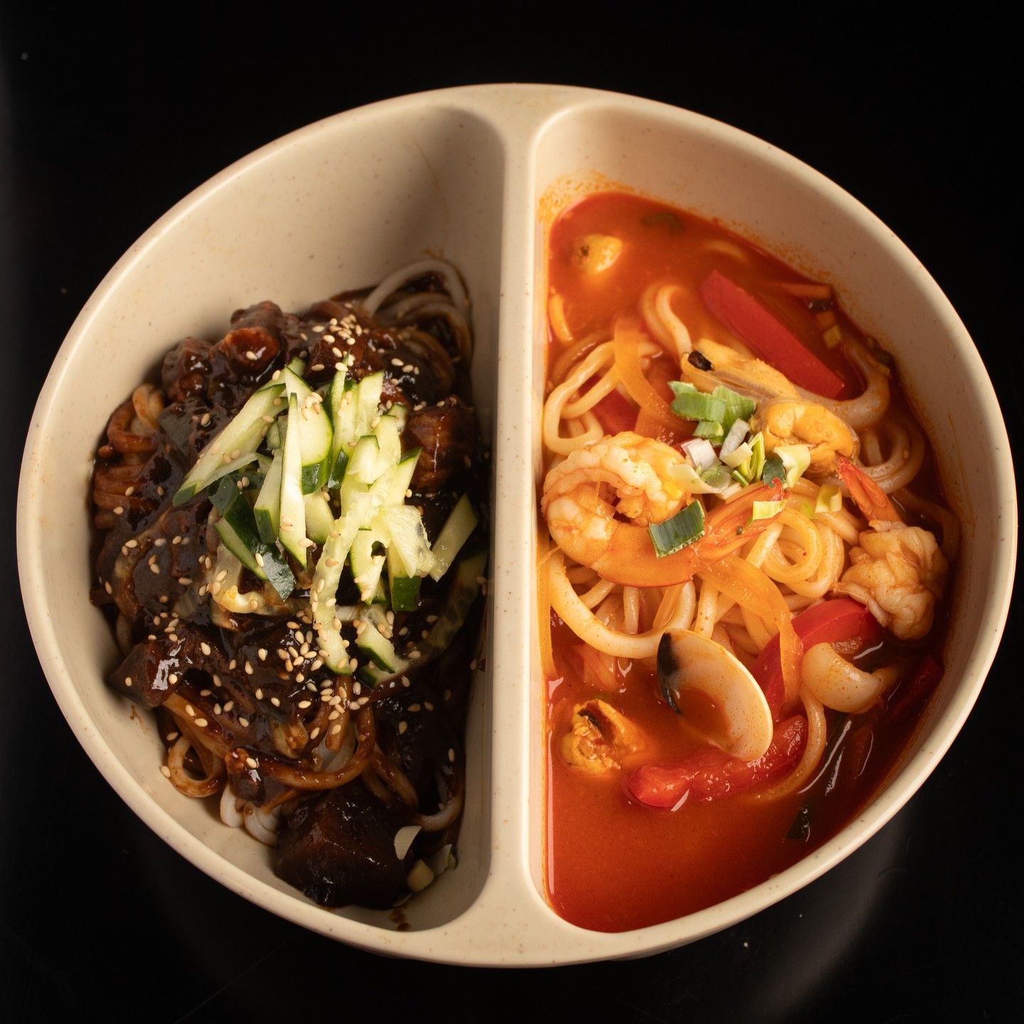 Un plato dividido con fideos: fideos con salsa oscura, cebolleta y sésamo a la izquierda; fideos en sopa roja con gambas a la derecha.
