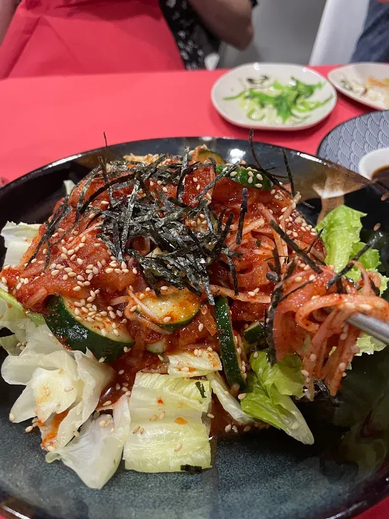 Plato picante de marisco con salsa roja, algas y col servido en un plato negro en la mesa de un restaurante