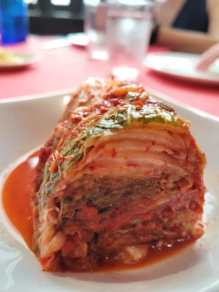 Una porción de lasaña en capas, cubierta con hierbas y salsa de tomate, en un plato blanco.